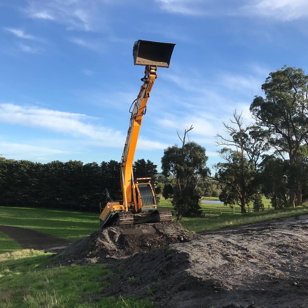 Excavator digging soil on a grassy hill.