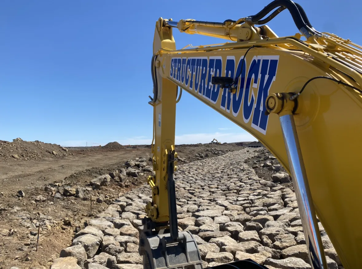 Excavator shaping rocky terrain under clear sky.
